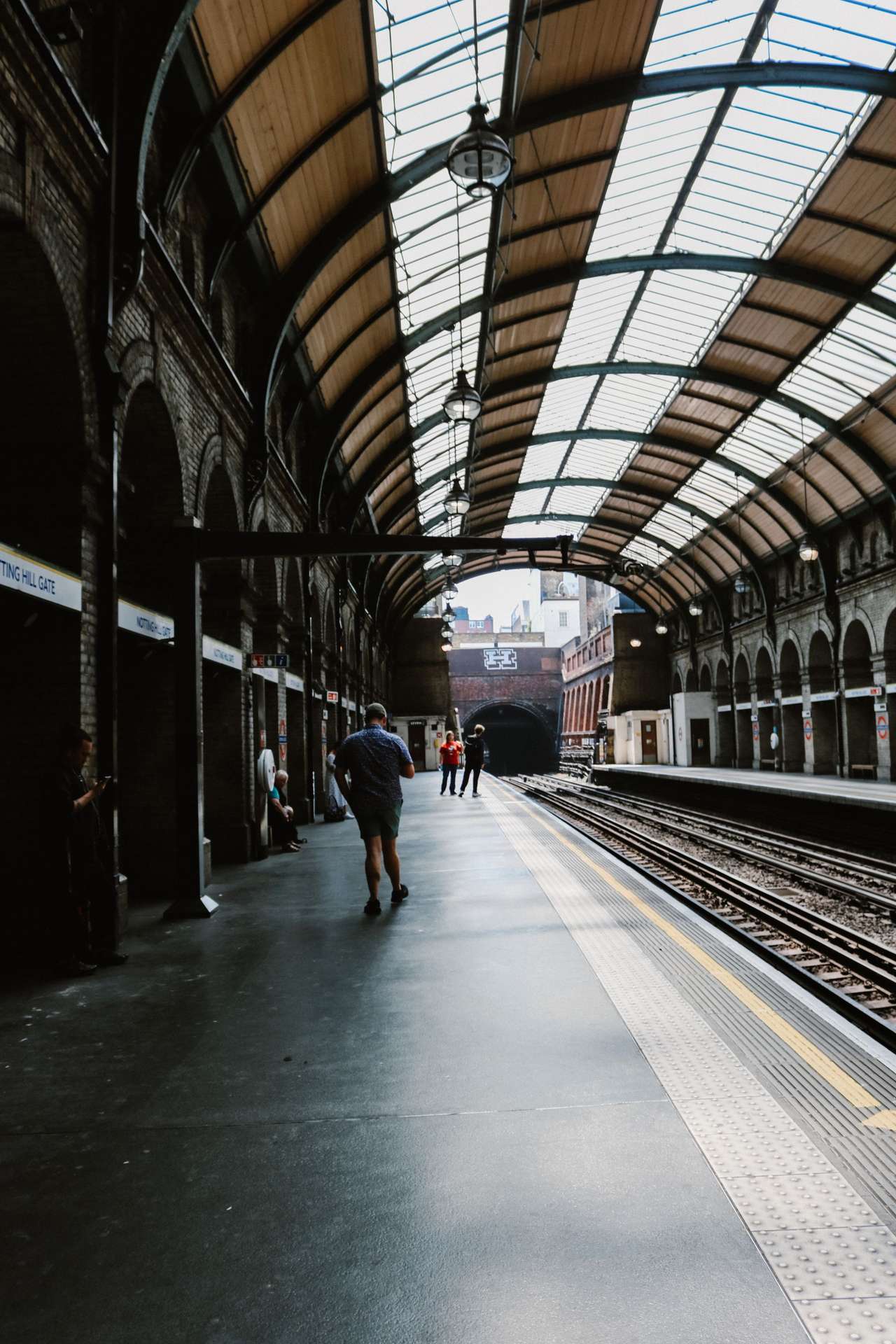 Passengers waiting on a long platform under a glass and iron roof at Notting Hill Gate