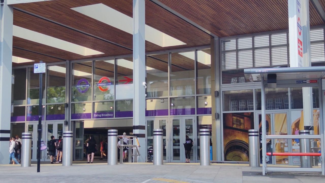 The glass and timber front of Ealing Broadway station, with people walking in and out of the entrance
