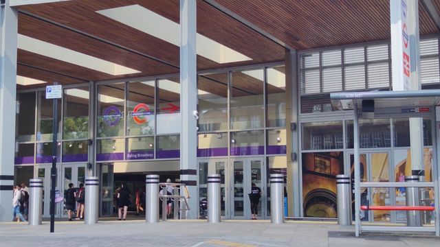 The glass and timber front of Ealing Broadway station, with people walking in and out of the entrance