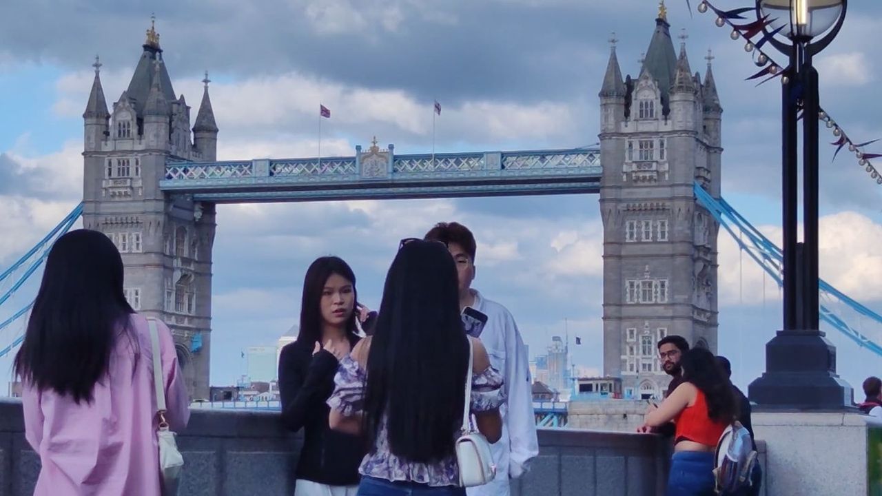 Visitors taking photos on the riverside with Tower Bridge behind