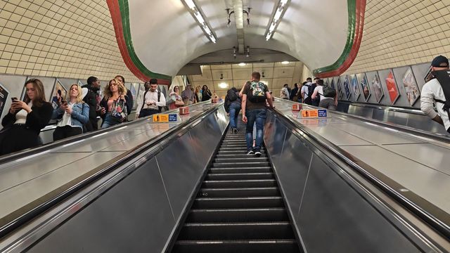 Long escalators inside Piccadilly Circus station, with passengers riding up and down beneath a curved tiled ceiling