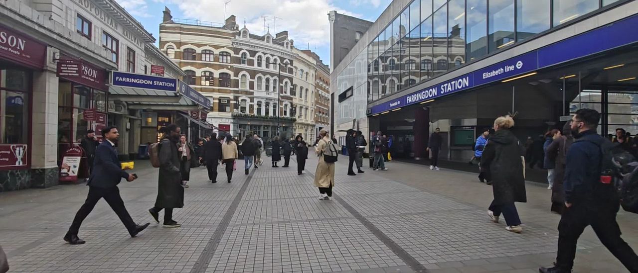 People walking along a pedestrian street past the Elizabeth line entrance at Farringdon station
