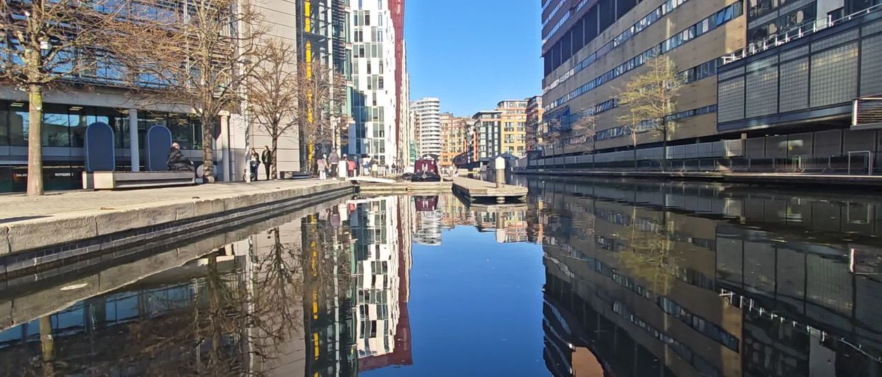 Modern buildings and a footbridge reflected in the still water of the canal at Paddington