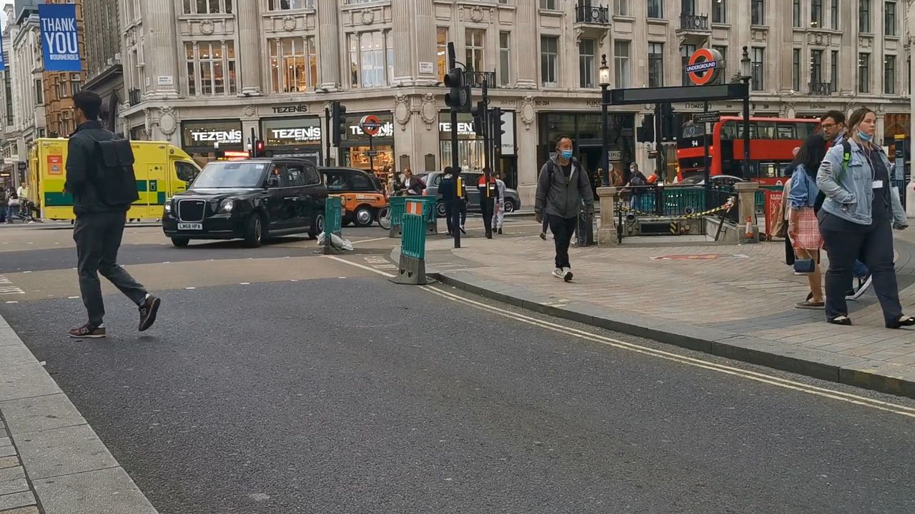 The road junction at Oxford Circus by day, with a black taxi, a red bus, people crossing and an Underground roundel over a station entrance