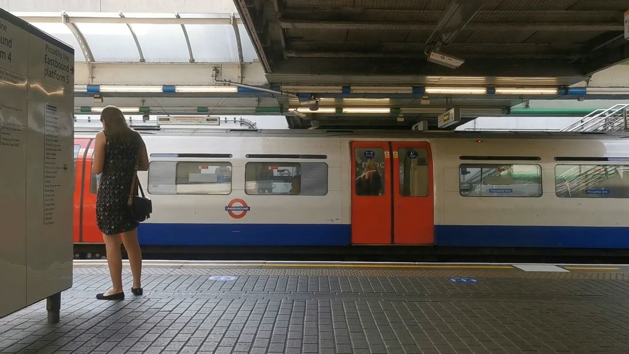 A Piccadilly line train standing at a covered platform at Hammersmith, with a passenger waiting beside it