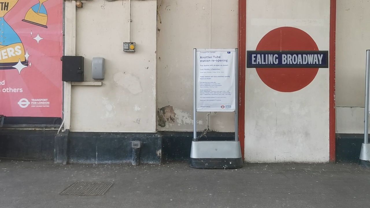 A large painted Ealing Broadway roundel on a wall outside the station, beside a notice board