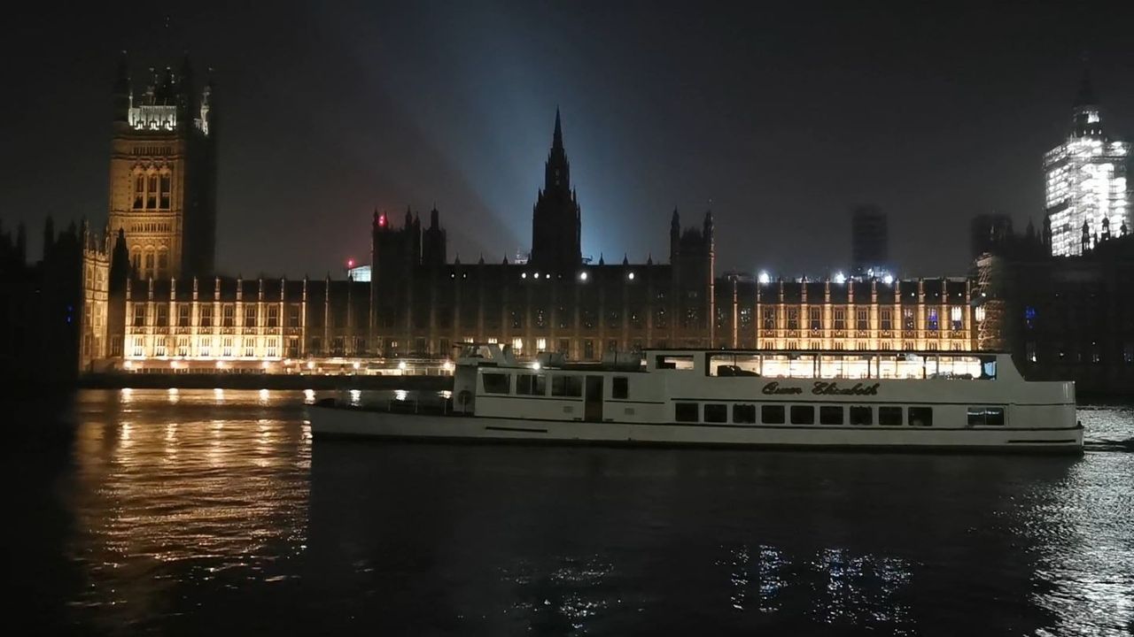 The Houses of Parliament lit up at night, with a boat on the dark river